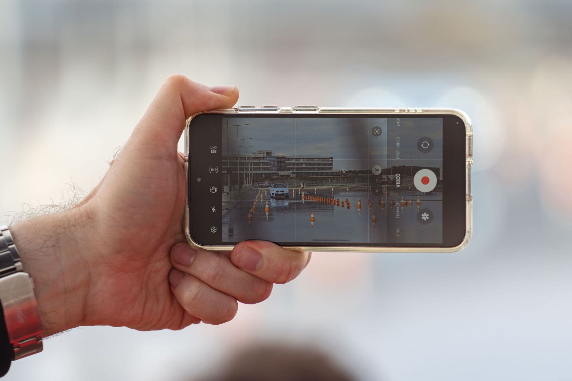A hand holding up a phone to film a car