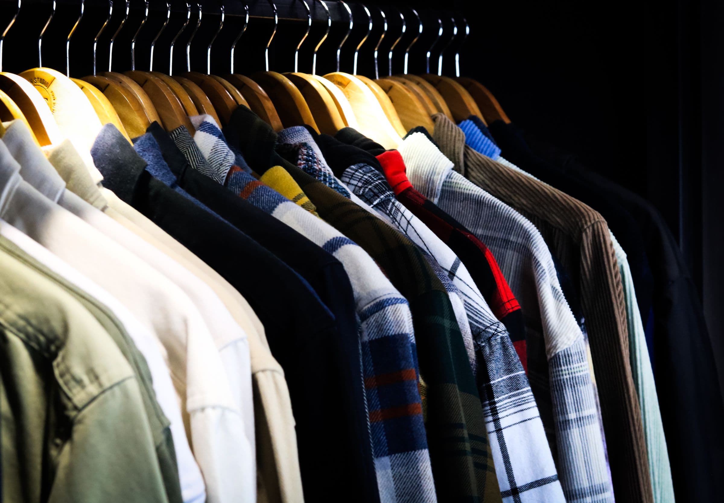 Men’s shirts on wooden hangers against a dark wall